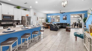 A modern kitchen with white cabinets, a central island with stools, and a dining area with a sofa and chairs.
