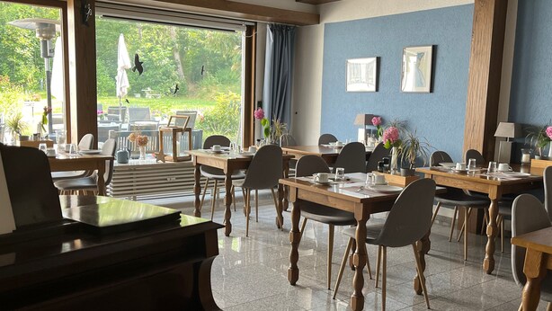 A dining area with wooden tables and chairs, a piano, and large windows with curtains. - Hotel Markgraf (Bad Bellingen)