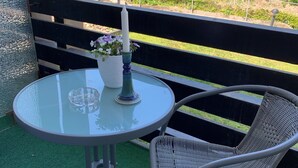A round glass table with a candle and a vase of flowers, a wicker chair, and a black railing. - Hotel Markgraf (Bad Bellingen)