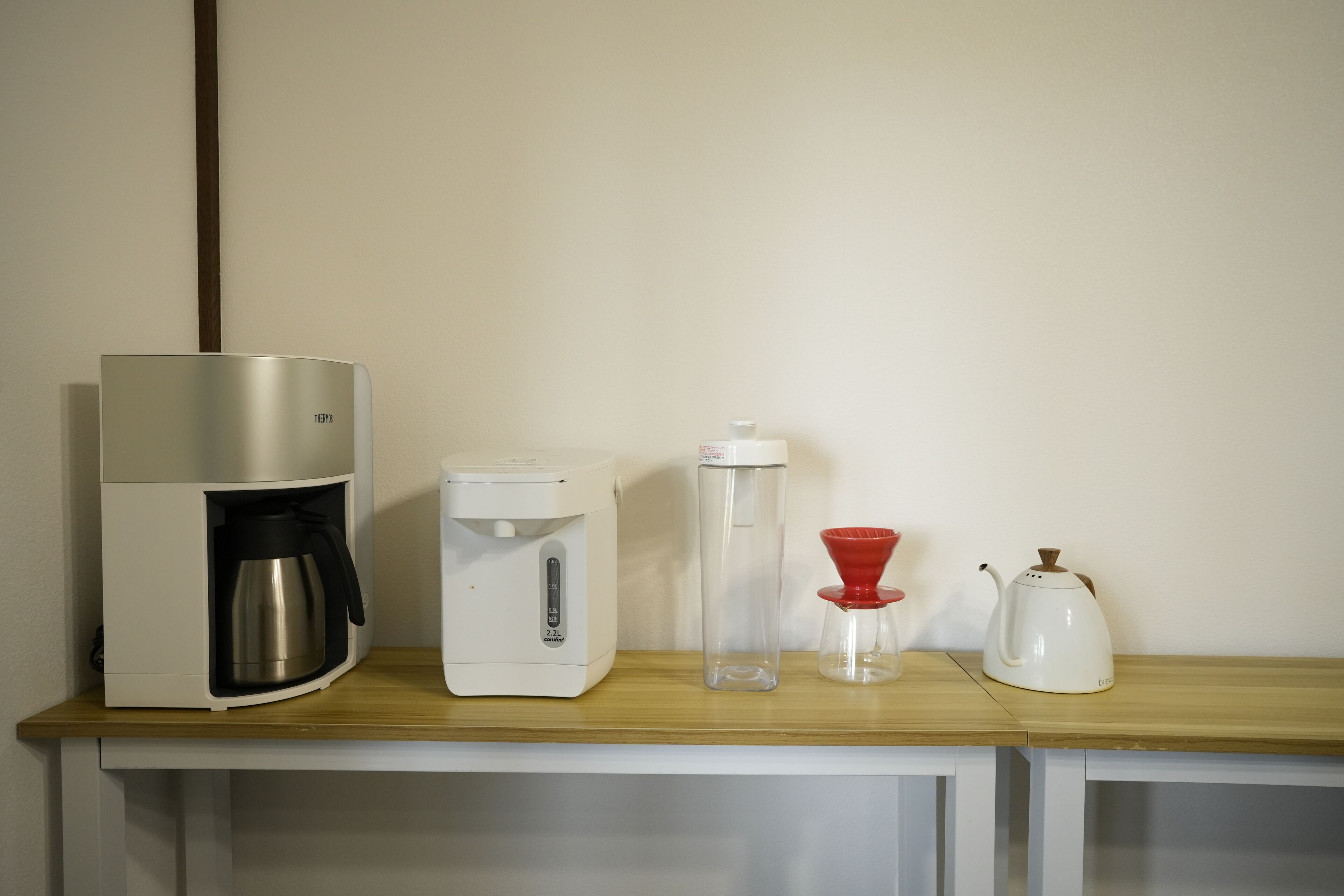 A kitchenette with a coffee maker, a water dispenser, a glass carafe, and a teapot on a wooden countertop.