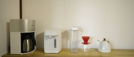 A kitchenette with a coffee maker, a water dispenser, a glass carafe, and a teapot on a wooden countertop.