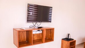 A room with a mounted TV on the wall, a wooden cabinet below, and a small coffee table to the right. - Hotel Brahma (Alappuzha)