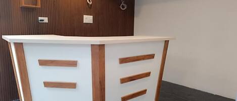 A reception desk with a white and wooden design, a wall-mounted air conditioner, and a wooden panel wall.