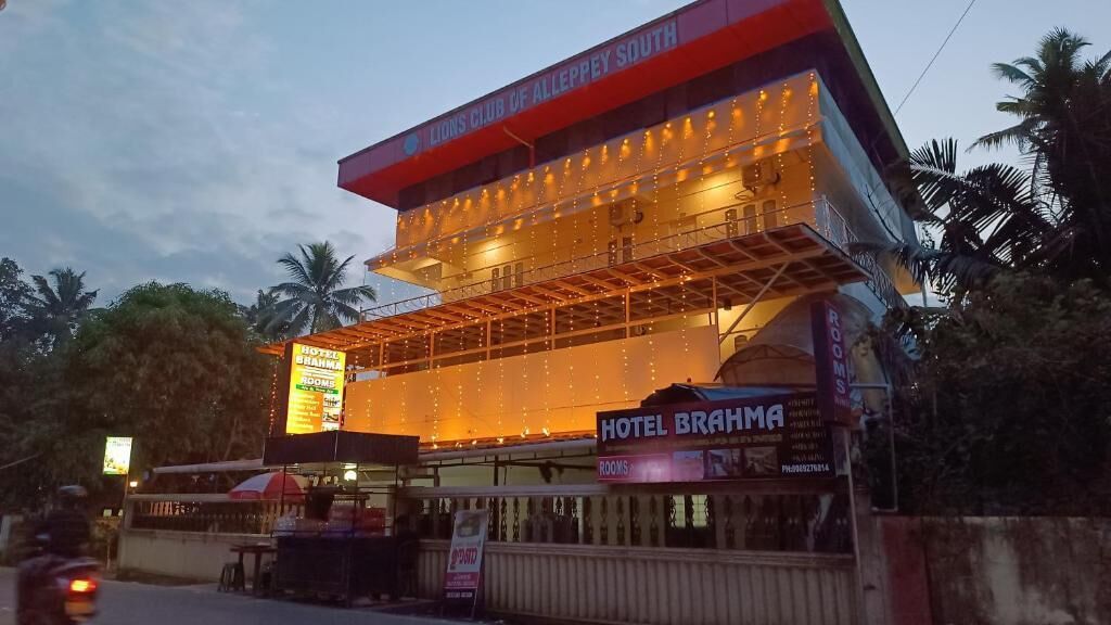 A multi-story hotel with a prominent sign for "Lions Club of Alleppey South" and "Hotel Brahma" indicating room availability.