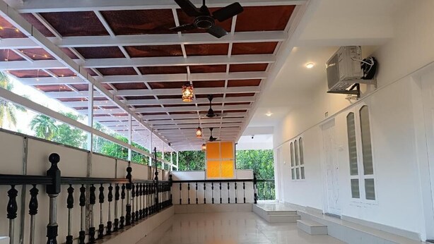 A spacious corridor with a tiled floor, a ceiling fan, and a series of hanging lights. - Hotel Brahma (Alappuzha)