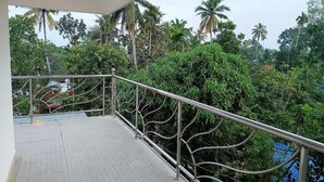 A balcony with a metal railing overlooking a lush garden with various trees and plants. - Hotel Brahma (Alappuzha)