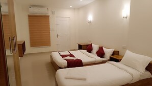 A hotel room with two beds, wooden headboards, white bedding, red pillows, bedside tables, a wooden wardrobe, and an air conditioning unit. - Hotel Brahma (Alappuzha)