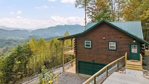 A log cabin with a green door and windows, a covered porch, and a view of mountains.