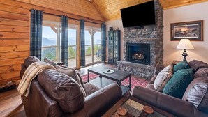 A cozy living room with a stone fireplace, leather sofas, and a large window overlooking a scenic view.