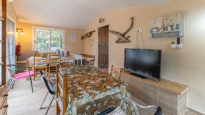 A dining area with a table covered in a floral tablecloth, a television on a stand, and a wall-mounted painting.