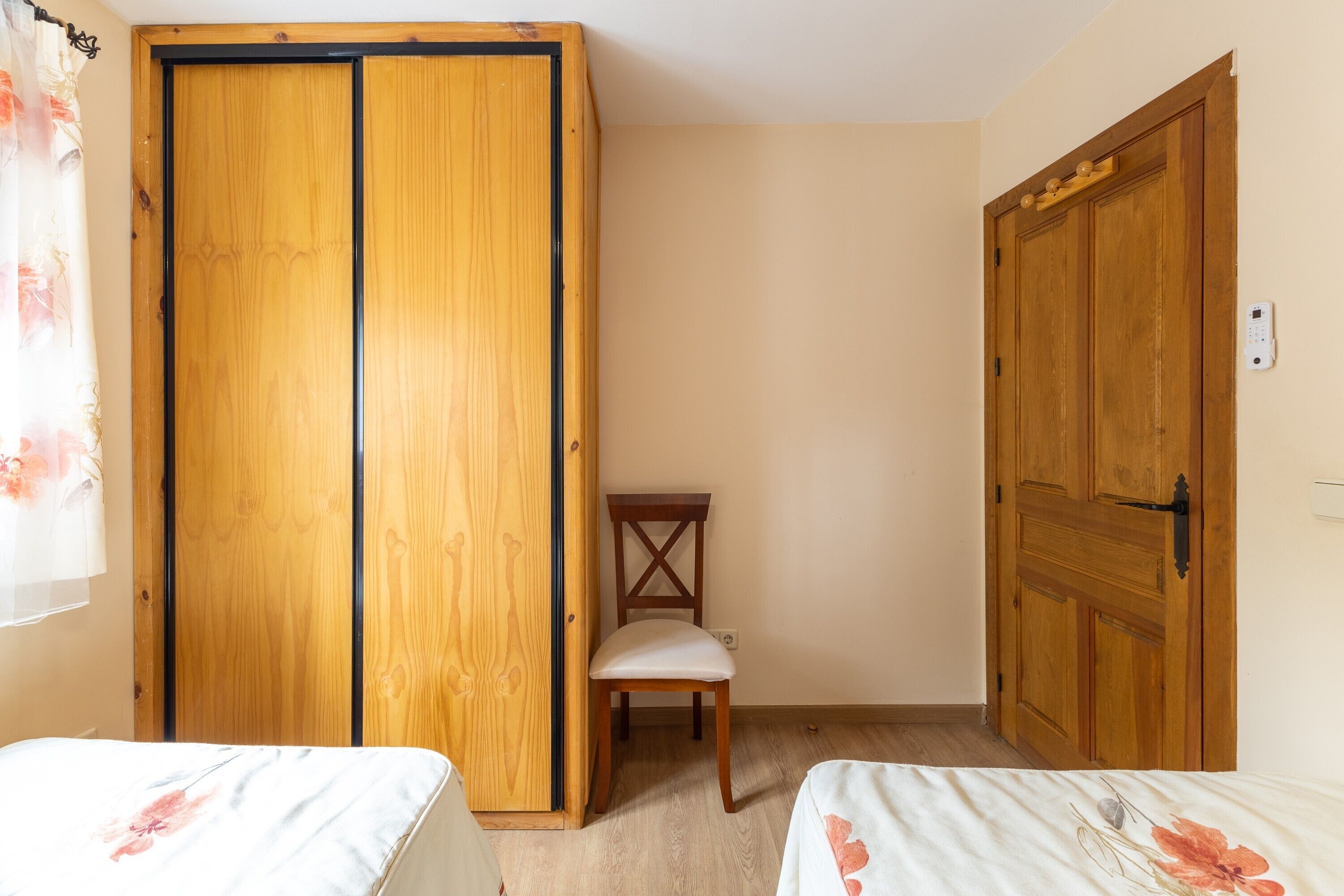 A bedroom with two beds, a wooden wardrobe, a wooden chair, and a door.