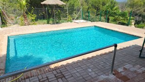 A rectangular swimming pool with clear blue water, surrounded by a brick deck and a metal safety railing.