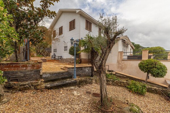 A white building with a stone staircase, a small garden, and a tree.