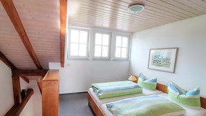 A bedroom with two beds, wooden beams, a window, and a painting.