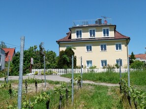 Un edificio a più piani con tetto in tegole rosse, una recinzione bianca e un vigneto in primo piano.