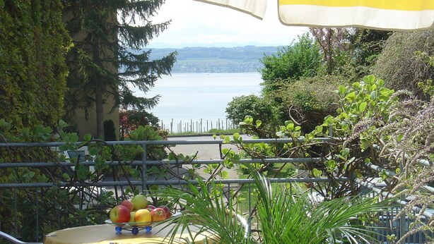 A balcony with a table holding fruit, a railing, and a view of a lake and distant city.