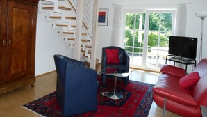 Una sala de estar con escaleras, un televisor, un sofá rojo, un sillón azul y un aparador de madera.