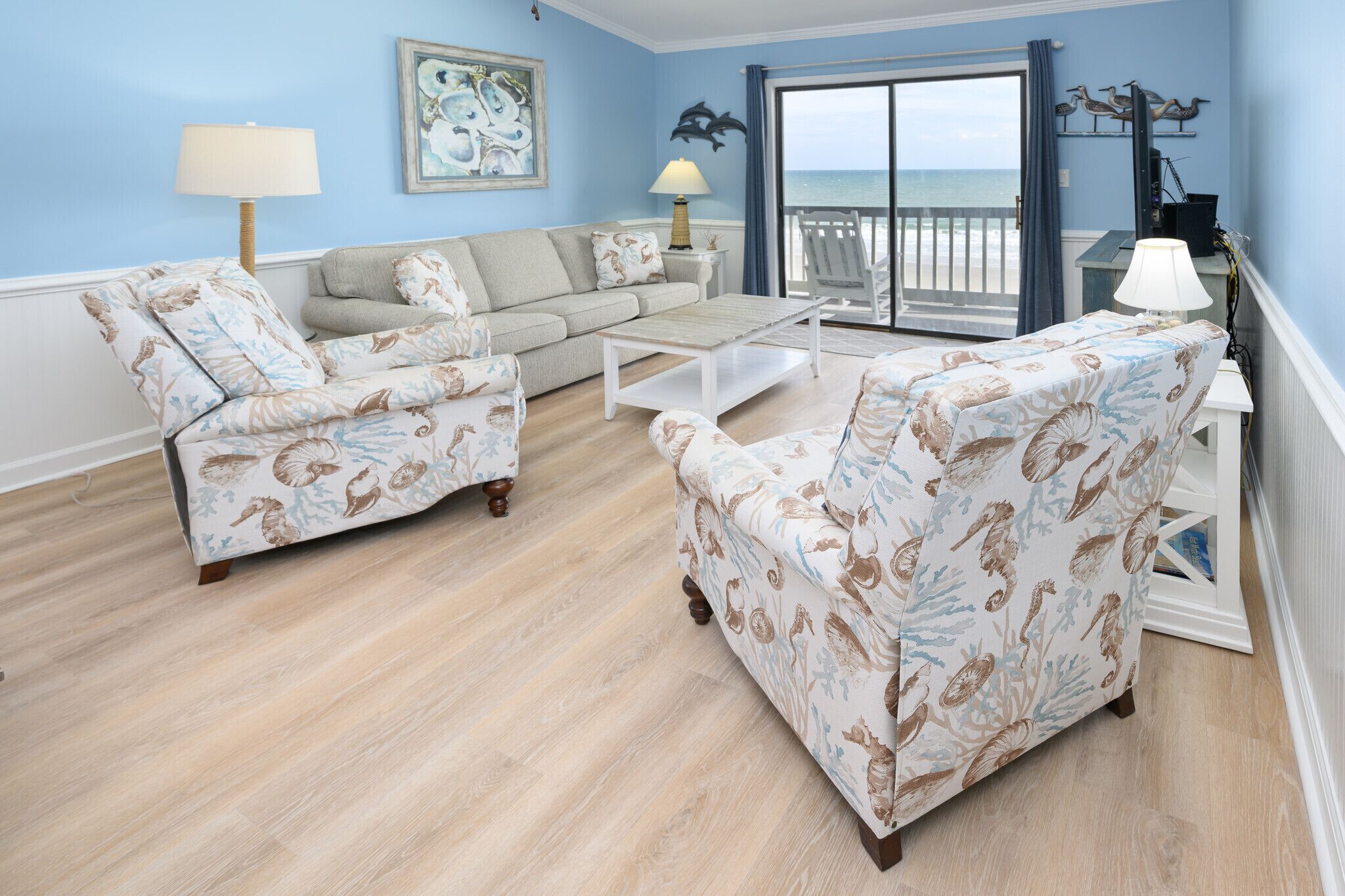 A living room with a sofa, two armchairs, a coffee table, and a view of the ocean through a sliding door.