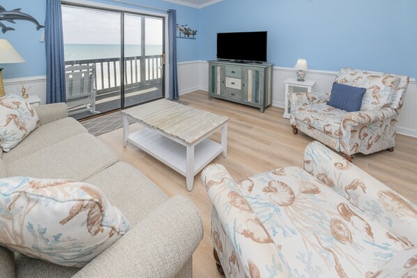 A living room with a sofa, armchair, and a television on a cabinet. - Oceanfront, Shared Pool - Surfwatch II 401 (Surfside Beach)