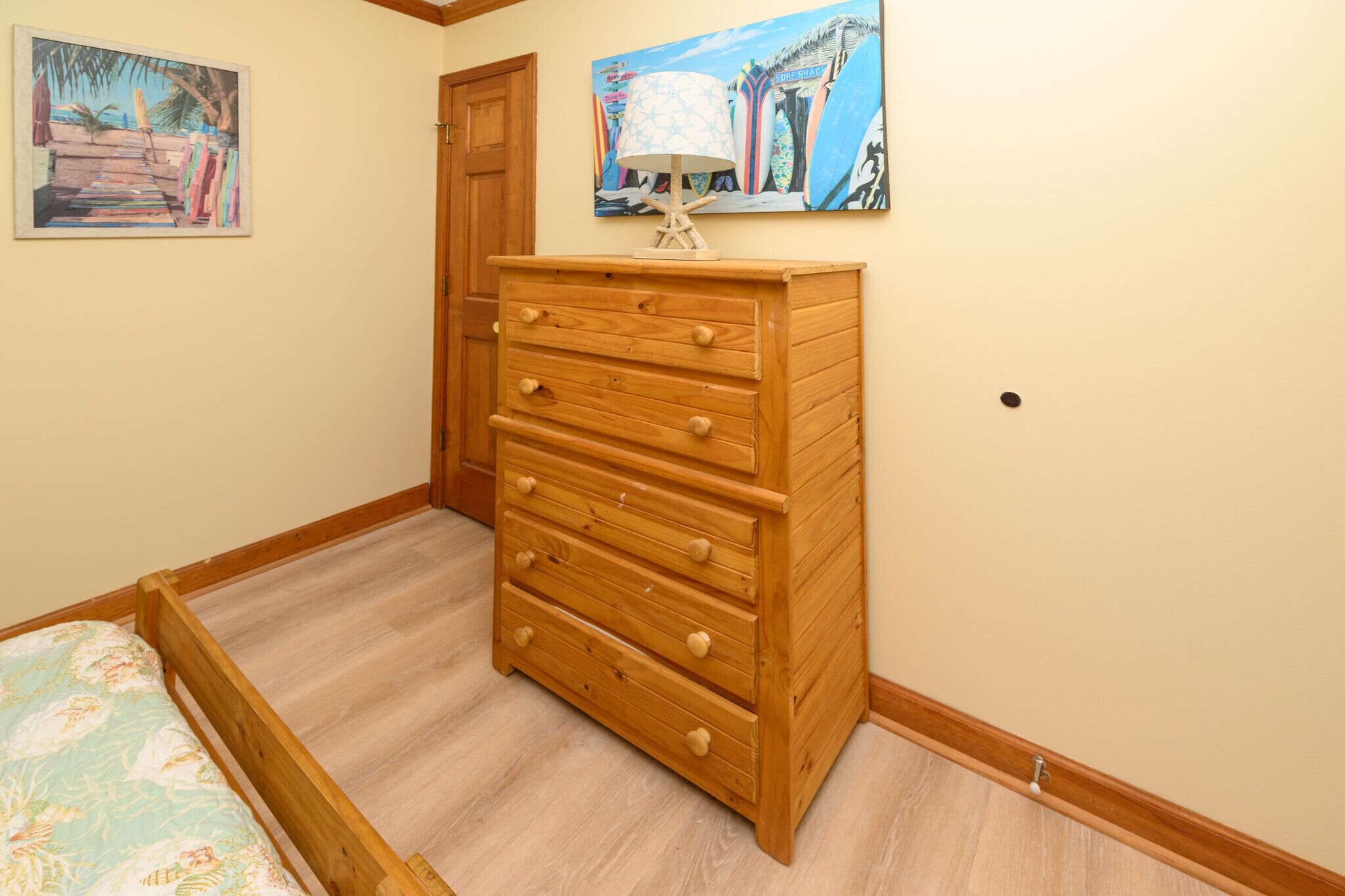 A bedroom with a wooden dresser, a bed with floral bedding, and two wall-mounted paintings.