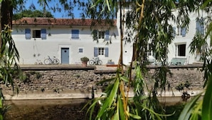 A white building with a stone wall in front, bicycles parked outside, and a clear blue sky. - Le Moulin De La Parenthèse (Sommières-du-Clain)