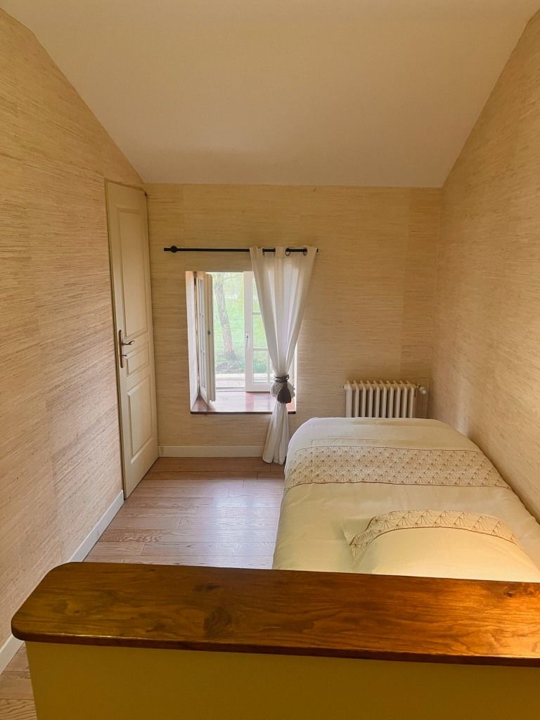 A bedroom with a wooden floor, a bed with a white duvet, a radiator, and a window with curtains.