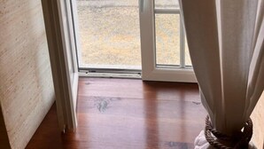 A room with a wooden floor, a sliding glass door leading outside, and a curtain partially drawn to the side. - Le Moulin De La Parenthèse (Sommières-du-Clain)