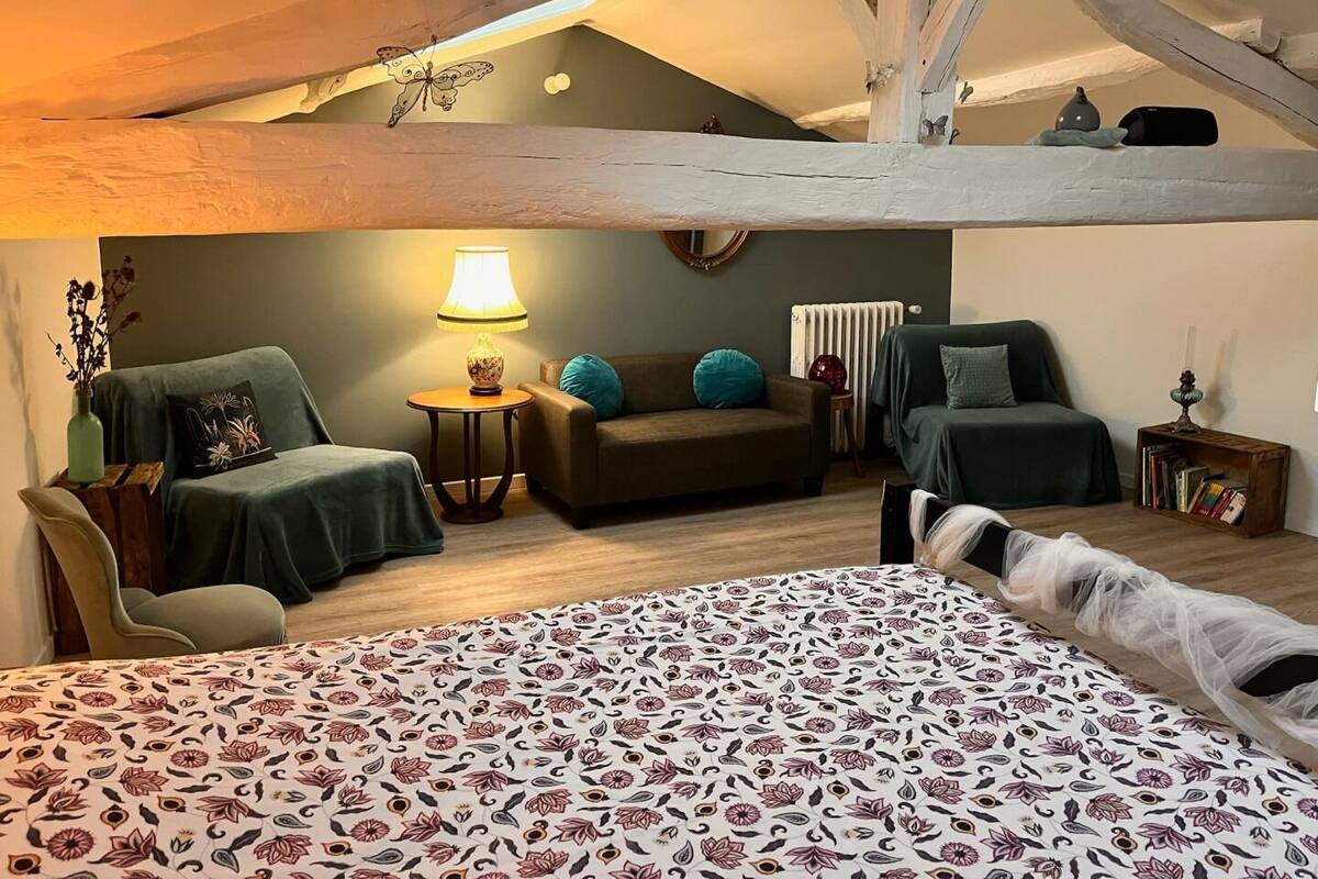 A cozy loft bedroom with a bed, two sofas, a small table, and a lamp.