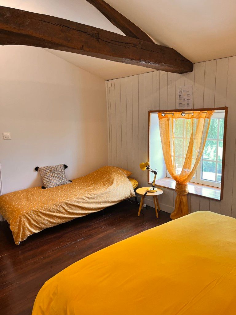 Un dormitorio con cama, una mesita, una lámpara y una ventana con cortinas.
