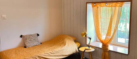 Un dormitorio con cama, una mesita, una lámpara y una ventana con cortinas.