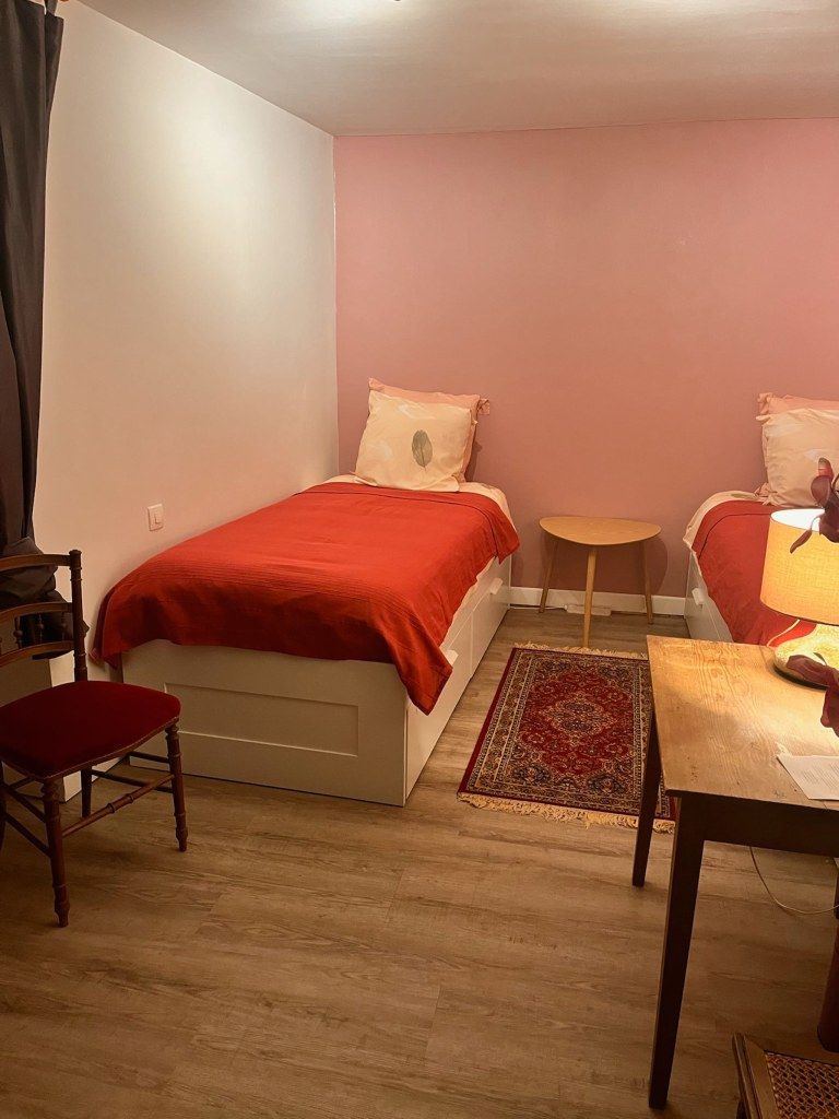 A small, cozy room with a bed, a chair, a small table, and a lamp.