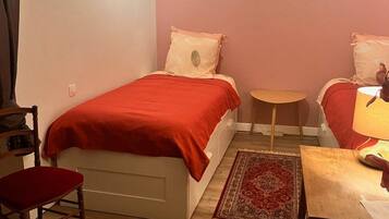 A small, cozy room with a bed, a chair, a small table, and a lamp.