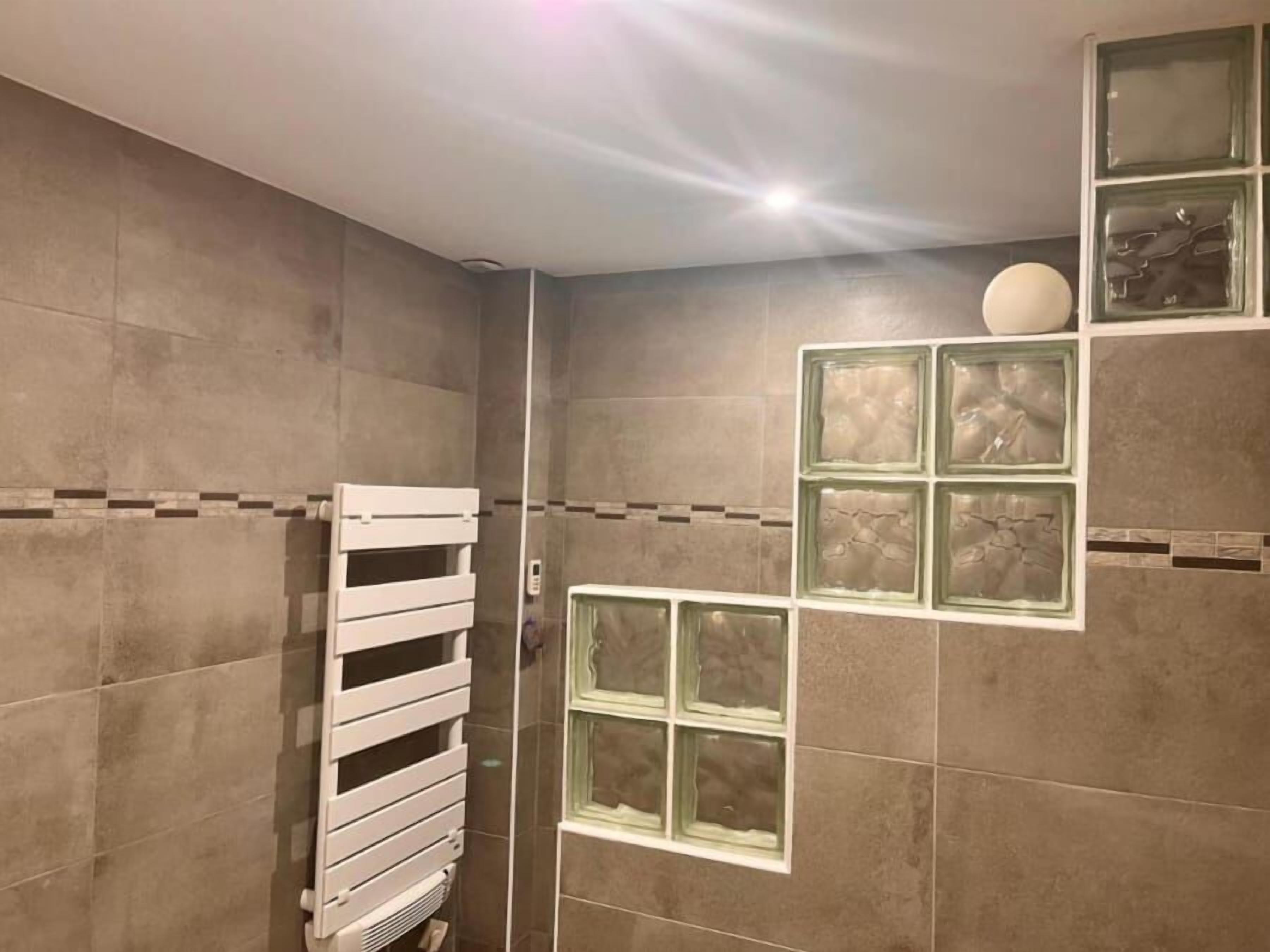 Un baño con toallero blanco, ducha y paneles de vidrio decorativos en la pared.