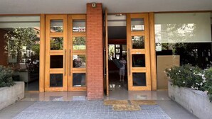 A building entrance with a brick pillar, large glass doors, and a tiled walkway. - Excelente Ubicación y Confort. (Las Condes)