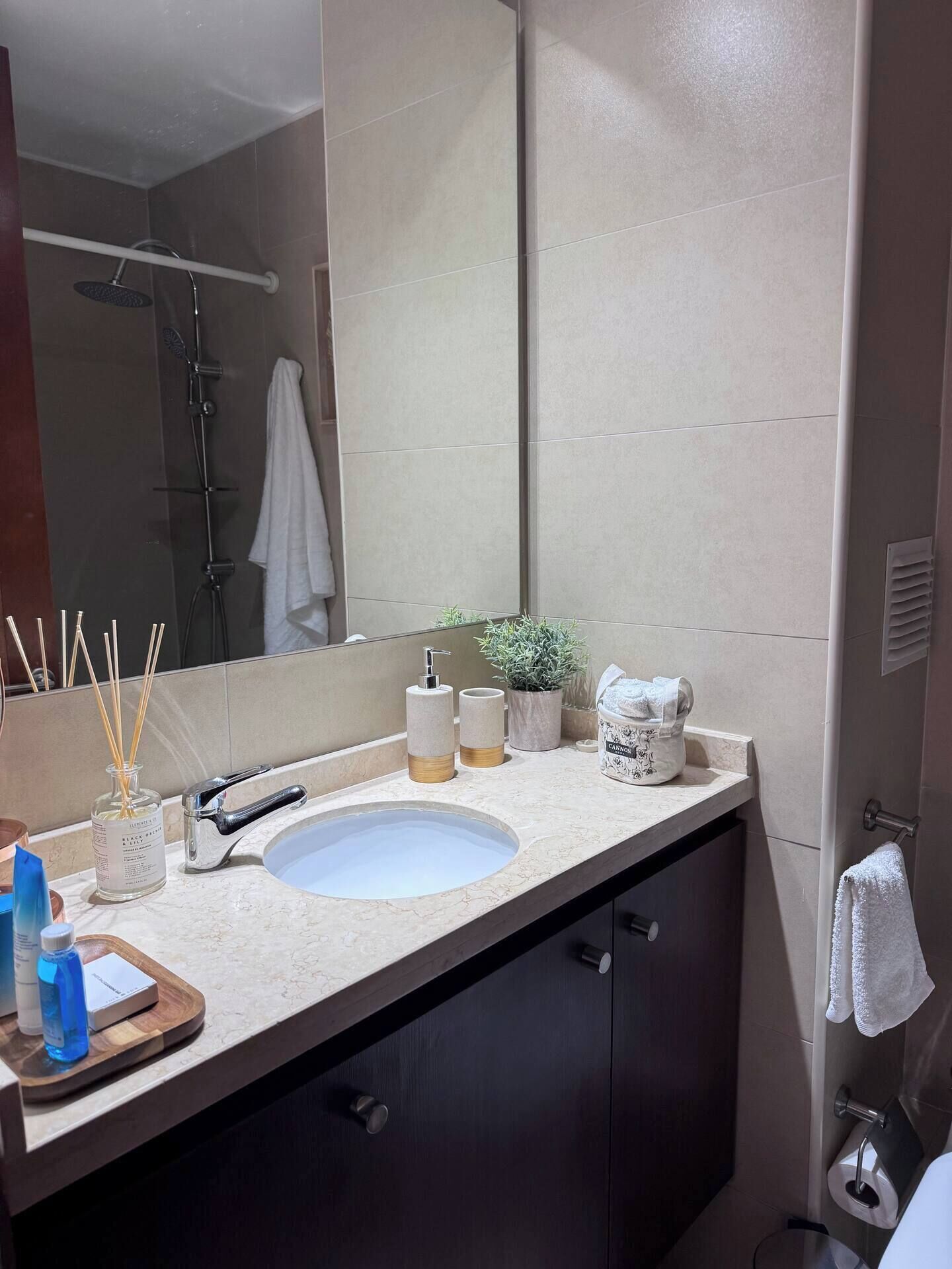 A modern bathroom with a large mirror, a sink, a shower, and a towel rack.