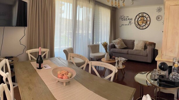 A living room with a dining table, chairs, a sofa, and a TV. - Excelente Ubicación y Confort. (Las Condes)