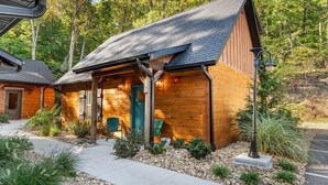 A wooden cabin with a sloped roof, a porch with chairs, and a small garden area with rocks and plants. - Family Cabin  • Hot Tub • Arcade• Near Thunder Ridge (Hollister)