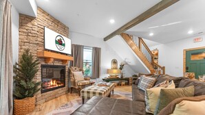 A cozy living room with a stone fireplace, leather sofa, and a staircase leading to an upper level. - Family Cabin  • Hot Tub • Arcade• Near Thunder Ridge (Hollister)