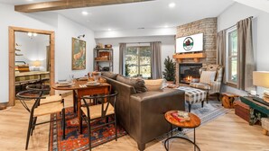 A cozy living room with a fireplace, a dining area, and a large mirror. - Family Cabin  • Hot Tub • Arcade• Near Thunder Ridge (Hollister)