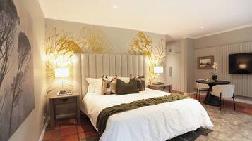 A modern bedroom with a large bed, two bedside tables with lamps, a small round table with a chair, and a TV on the wall.