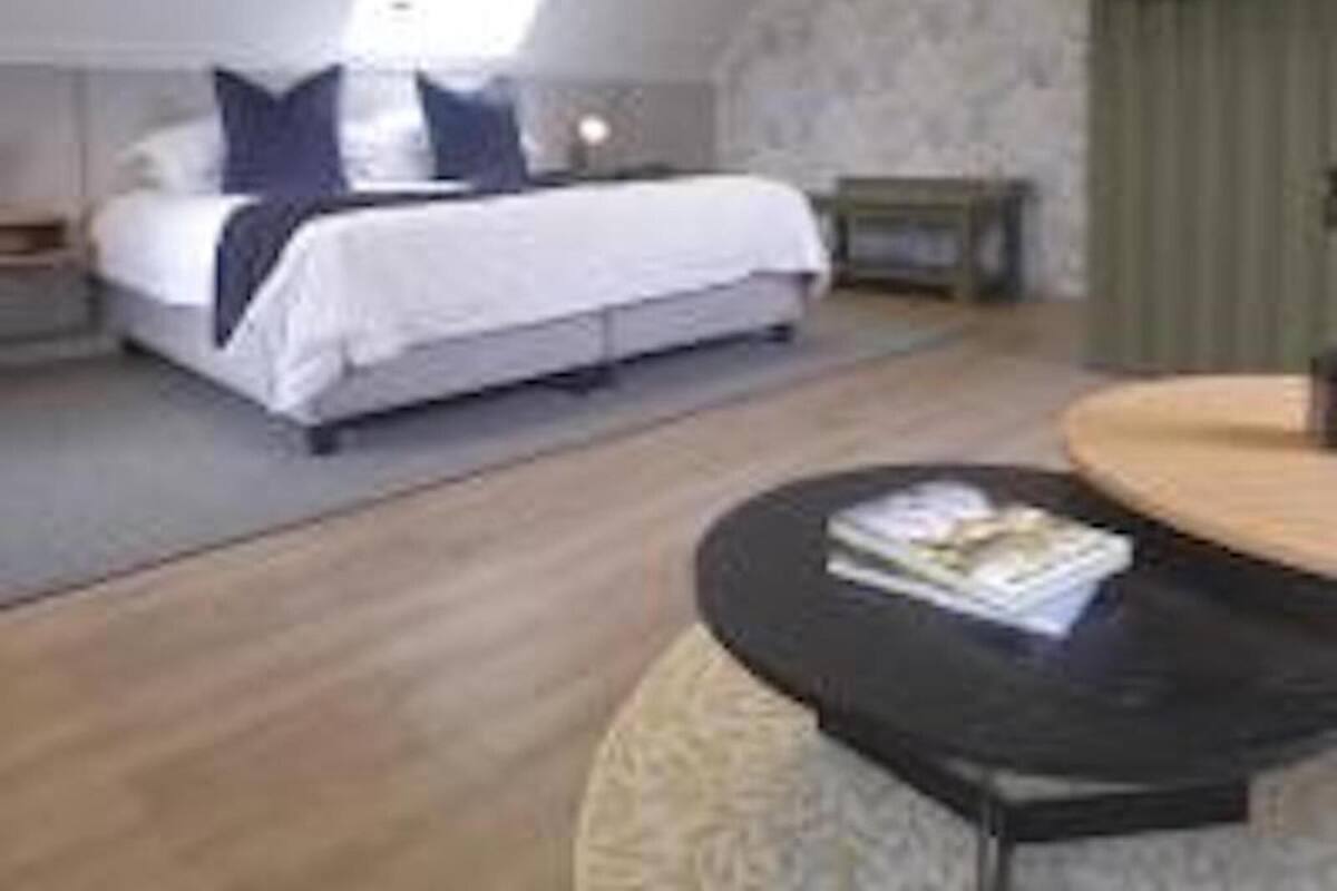 Un dormitorio con cama, mesitas de noche, una mesa redonda y un televisor montado en la pared.