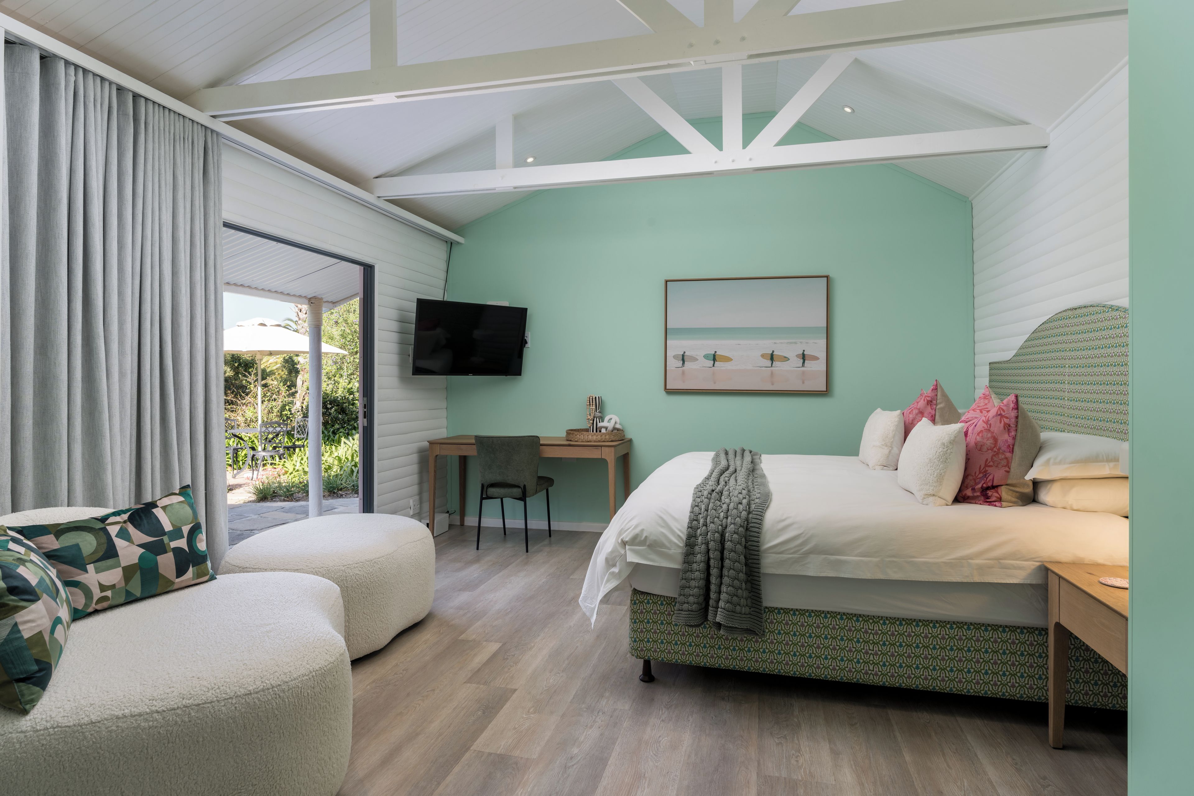 Ein Schlafzimmer mit Bett, Schreibtisch, Stuhl, Fernseher und Blick ins Freie.