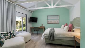 A bedroom with a bed, a desk, a chair, a TV, and a view of the outdoors.