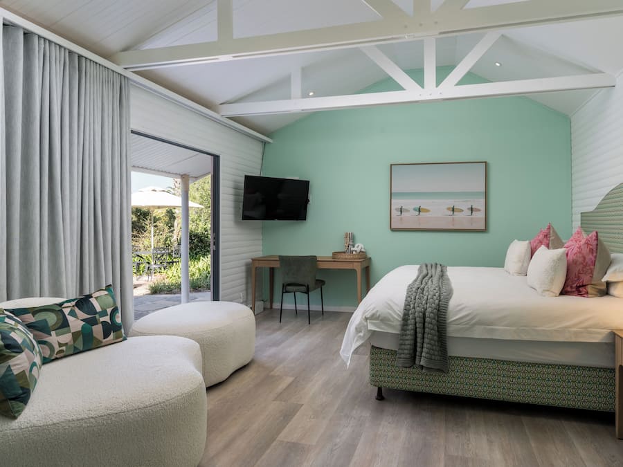 A bedroom with a bed, a desk, a chair, a TV, and a view of the outdoors.