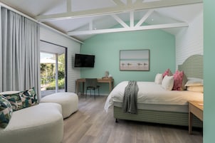 Quarto com cama, escrivaninha, cadeira, TV e vista para o exterior.