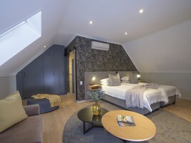 Un dormitorio moderno con techo inclinado, una cama con cabecera, un sofá, una mesita de centro y una pequeña mesita auxiliar.