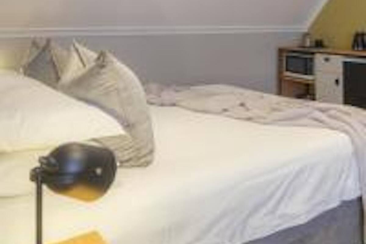 Un dormitorio con cama, almohadas, una lámpara y un escritorio pequeño con televisión.