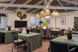 Espaço de refeições interno com mesas, cadeiras, arte decorativa nas paredes e luminárias de vime suspensas.