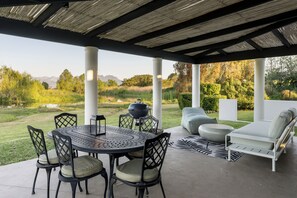 Una veranda esterna con un tavolo rotondo, sedie, un barbecue e una zona relax.
