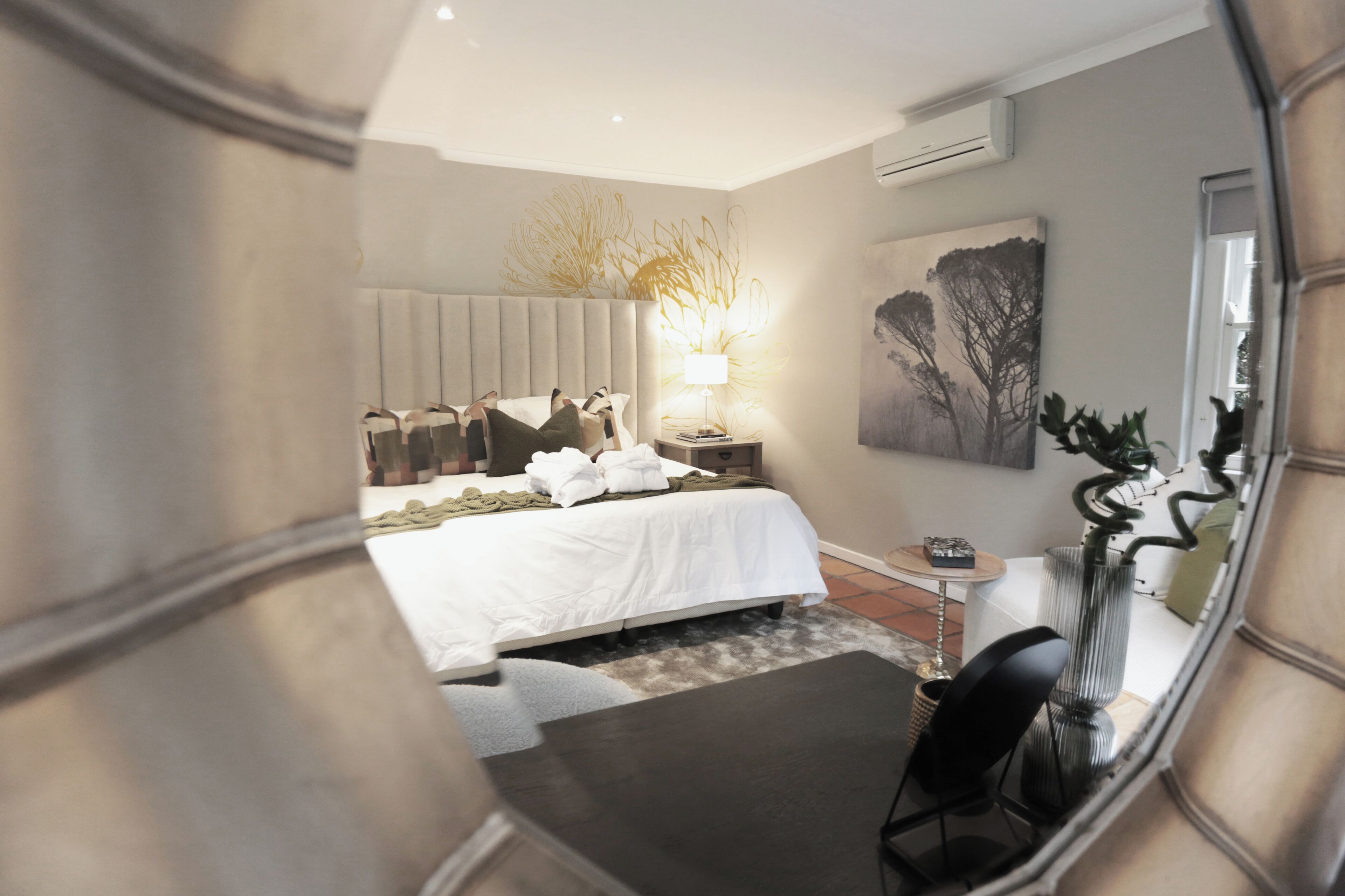 A modern hotel room with a large bed, a bedside table with a lamp, a small table, and a chair.